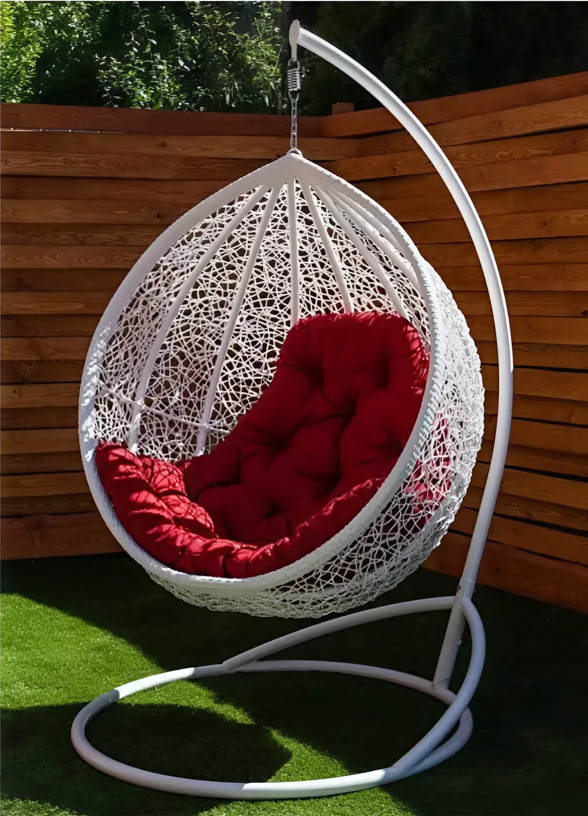 Luna hanging egg chair in white rattan with a deep red cushion in a sunlit backyard corner.
